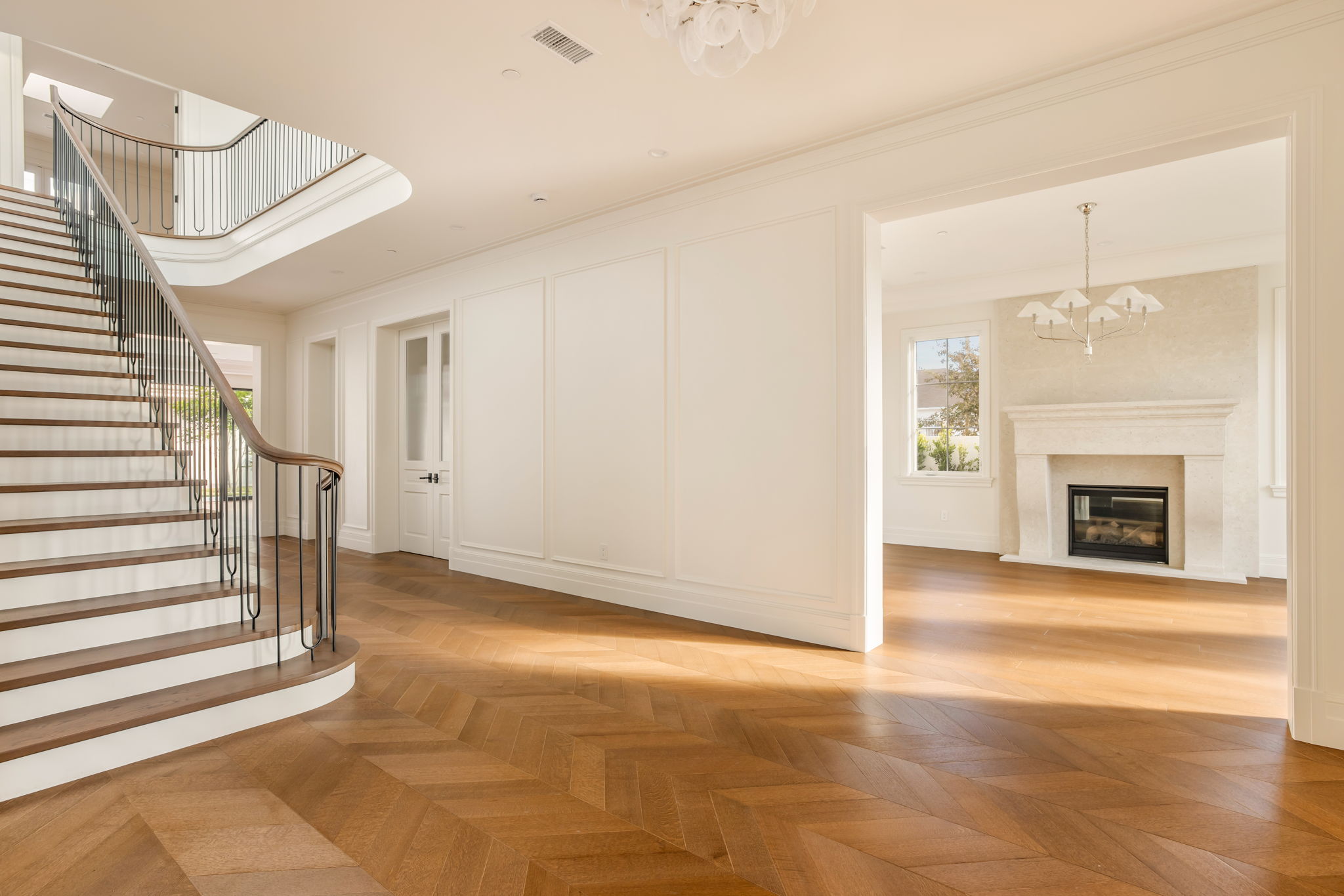 The Magnolia House entry hall with chevron floors and staircase, opening to living room fireplace