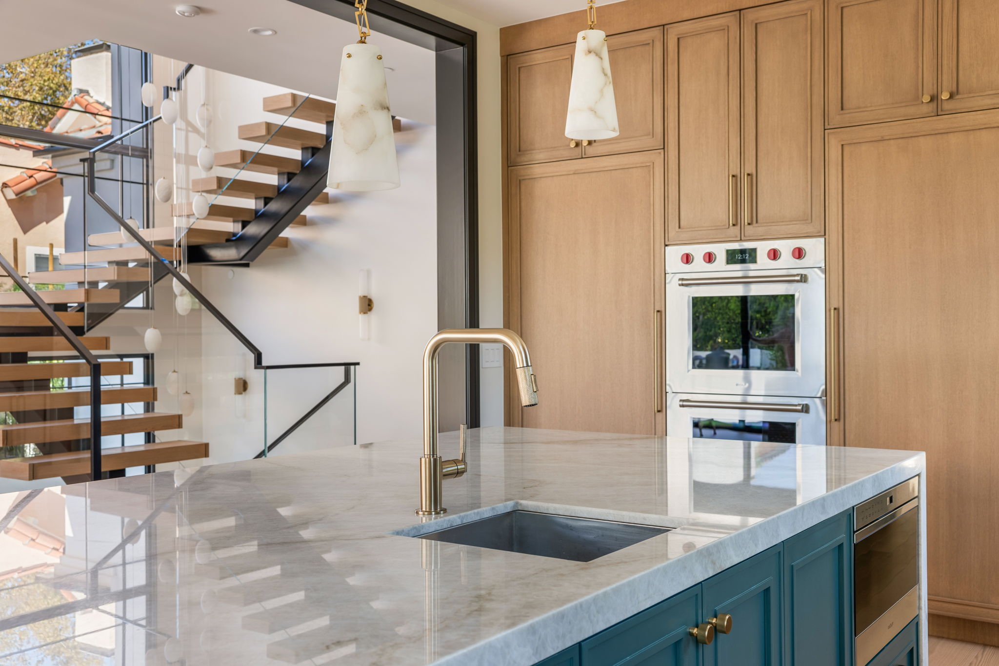The Verdigris House kitchen island detail with brass faucet and floating staircase beyond
